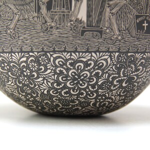 May include: Black and white ceramic bowl with a detailed design of skeletons and flowers. The bowl has a scalloped edge and a smooth, rounded bottom.