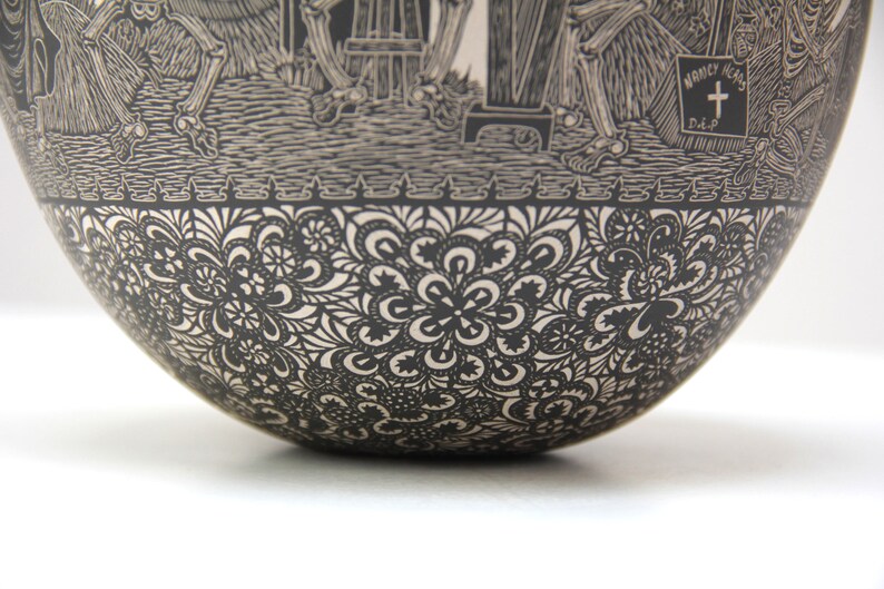 May include: Black and white ceramic bowl with a detailed design of skeletons and flowers. The bowl has a scalloped edge and a smooth, rounded bottom.