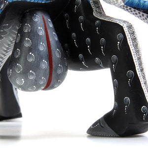 May include: A black wooden animal figurine with white and blue painted details. The figurine has a large, round, grey body with a red stripe down the centre. The legs are decorated with a white and black pattern.