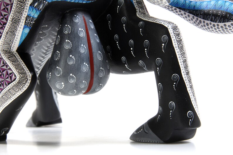 May include: A black wooden animal figurine with white and blue painted details. The figurine has a large, round, grey body with a red stripe down the centre. The legs are decorated with a white and black pattern.