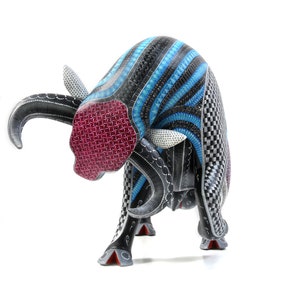 May include: A wooden bull sculpture carved in black, blue and white with intricate geometric patterns. The bull's head is lowered, and its horns are curved. The bull's eyes are painted white, and its nose is painted red.