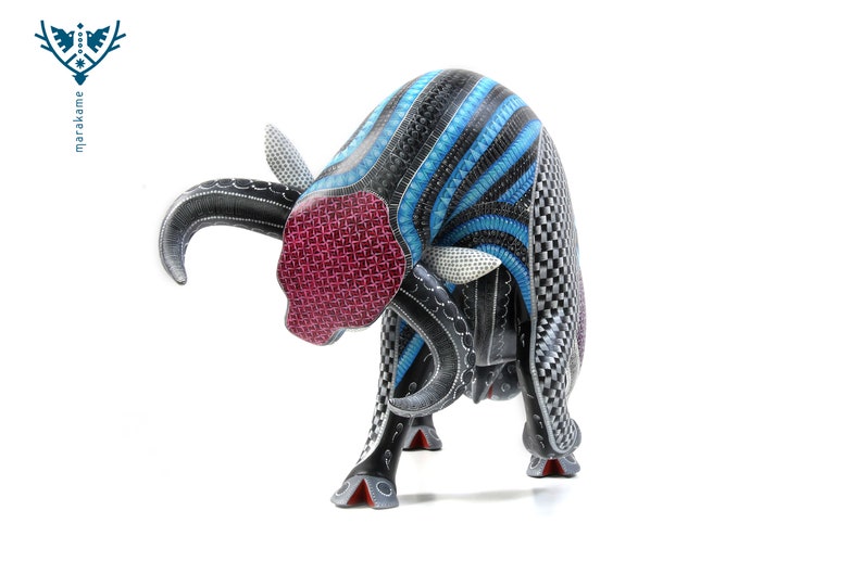 May include: A wooden bull sculpture carved in black, blue and white with intricate geometric patterns. The bull's head is lowered, and its horns are curved. The bull's eyes are painted white, and its nose is painted red.