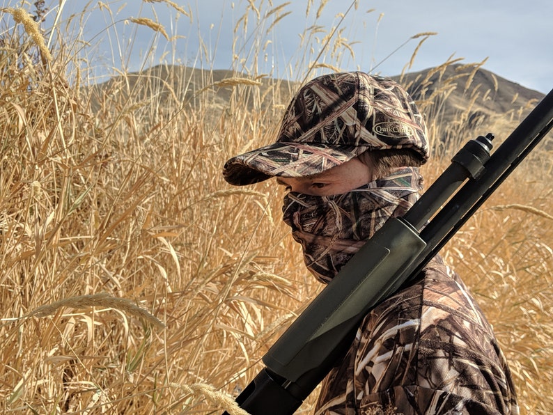 K&ouml;nnte beinhalten: Eine Person in Tarnkleidung und einer Tarnkappe mit dem Schriftzug "Duck Commander". Die Person h&auml;lt eine Schrotflinte.