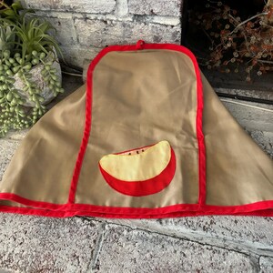 May include: A brown oven mitt with a red trim and a red apple applique. The apple is yellow with a red outline.
