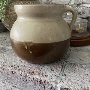 May include: A brown and white glazed ceramic pitcher with a handle. The pitcher has a rounded body and a wide mouth.