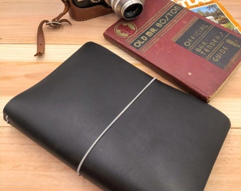 May include: A vintage silver and black camera with a brown leather case rests on a wooden surface, alongside a black leather journal and two antique books. One book is titled "Old Mr. Boston Official Bar Tender Guide."