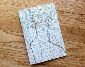 May include: A folded paper map of the state of Minnesota with major highways and cities labeled. The map is on a light brown wooden surface.