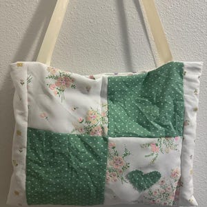 Może przedstawiać: Zielona i biała torba typu tote w patchworku z kwiatowym materiałem i białymi kropkami. Torba ma kremowy pasek.