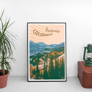 Op de afbeelding: Een ingelijste kunstdruk met een berglandschap in Breckenridge, Colorado. De print toont een schilderachtig uitzicht met groene en oranje bomen, blauwe bergen en de tekst "Breckenridge Colorado" in een vintage stijl.