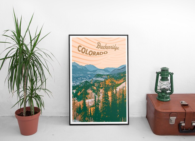 Op de afbeelding: Een ingelijste kunstdruk met een berglandschap in Breckenridge, Colorado. De print toont een schilderachtig uitzicht met groene en oranje bomen, blauwe bergen en de tekst "Breckenridge Colorado" in een vintage stijl.