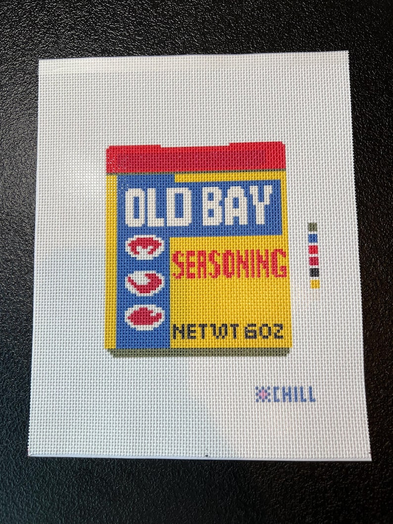 May include: A needlepoint design featuring a yellow, blue, and red box of Old Bay Seasoning. The text "OLD BAY SEASONING" is prominently displayed, with "NET WT 6 OZ" below. The word "CHILL" is also present.