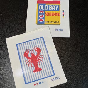 May include: Two needlepoint canvases. One features the Old Bay seasoning box with text and a net weight of 6 oz. The other canvas has a red lobster over blue and white stripes. Both have the word "CHILL".