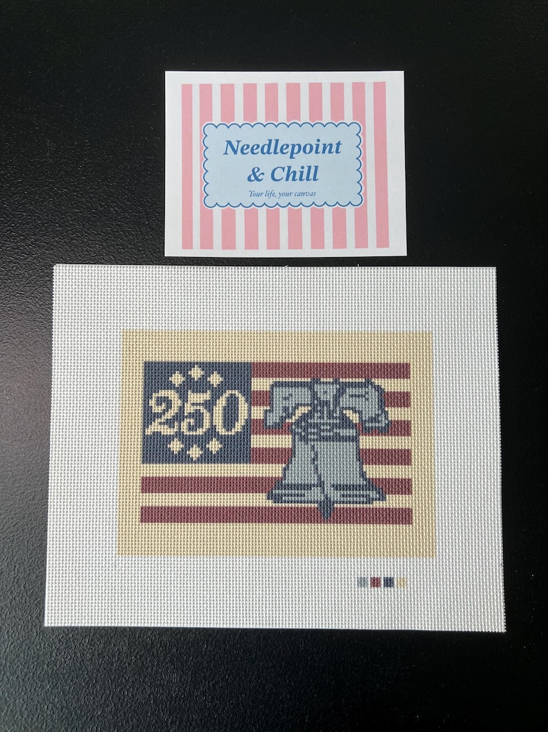 May include: Needlepoint canvas featuring a patriotic design with the Liberty Bell and the number "250" on a flag. The canvas is white with a rectangular design in shades of red, blue, and beige. The text "Needlepoint & Chill" is also visible.