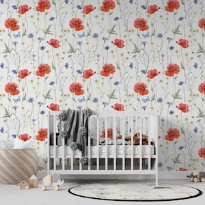 May include: A white cot set against a floral wallpaper with red poppies, blue cornflowers, and butterflies. A woven basket, wooden toys, and a round rug with a world map design create a nursery scene.
