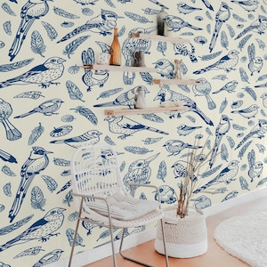 May include: A white wicker chair with a white cushion sits in a room with a wall covered in a blue and white bird pattern wallpaper. The wallpaper features a variety of bird species, including cardinals, robins, and sparrows. The wallpaper is a great way to add a touch of nature to any room.