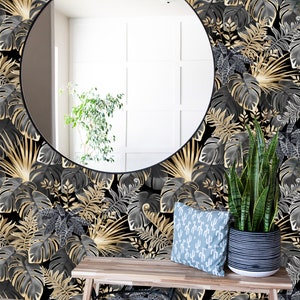 May include: A black and gold tropical leaf wallpaper with a round mirror, a wooden bench, a black wire basket, a potted plant, and a blue throw pillow with a cactus pattern.