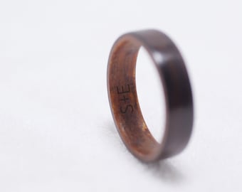 May include: A dark brown wooden ring with a light brown inner band. The ring has the initials "S+E" engraved on the inside.