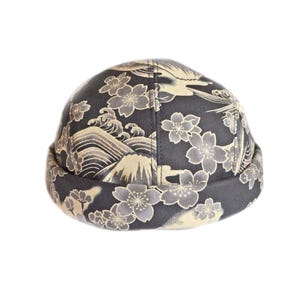 May include: A dark gray cap with a Japanese-inspired design featuring cherry blossoms, waves, and a bird. The cap has a rolled brim and a rounded crown. The pattern is in shades of gray, beige, and white.