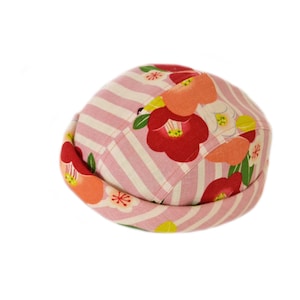 May include: A round, fabric hat with a pink and white striped pattern. The hat is decorated with red, orange, and yellow floral designs. The hat is a unique accessory.