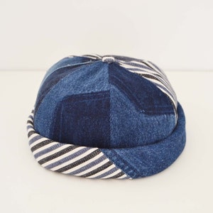 Peut inclure: Casquette en jean bleu avec un motif patchwork. Le bord est rayé bleu, noir et blanc. La couronne est faite de différentes pièces de jean, donnant un aspect texturé. Cet accessoire est un ajout élégant à toute tenue.