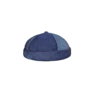 May include: A blue denim beanie with a patchwork design. The beanie is made of different shades of blue denim and has a folded brim.
