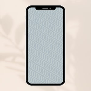 Op de afbeelding: Een zwarte smartphone met een lichtblauw golvend patroon op het scherm. De telefoon staat verticaal tegen een beige achtergrond, met een schaduw van een blad in de linkerbovenhoek.