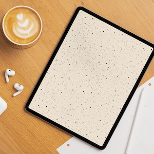 Op de afbeelding: Een digitale tablet met een gespikkeld crèmekleurig scherm, een kop koffie met latte art, draadloze oortelefoons en een stylus op een houten oppervlak. De scène suggereert een werkplek of een moment van ontspanning.