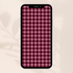 Op de afbeelding: Een smartphone met een scherm dat een bordeauxrood en roze ruitpatroon weergeeft. De telefoon heeft een zwarte rand en een inkeping aan de bovenkant. De achtergrond is lichtbeige.