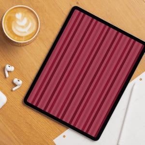 Op de afbeelding: Een digitale tablet met een scherm met verticale strepen in roodtinten. Een kopje koffie met latte art, witte draadloze oortelefoons en een stylus liggen op een houten oppervlak.