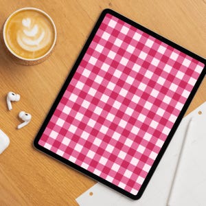 Puede incluir: Una tableta digital muestra un patrón de cuadros rosa y blanco. Una taza de café con arte latte, auriculares inalámbricos y un lápiz óptico están sobre una superficie de madera. La escena está tomada desde arriba.