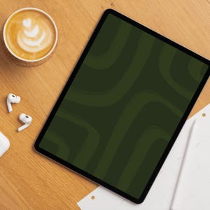 Op de afbeelding: Een digitale tablet met een donkergroen abstract ontwerp, een kopje koffie met latte art en witte draadloze oortelefoons op een houten oppervlak. Een witte stylus en een notitieblok zijn ook aanwezig.
