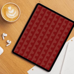 Op de afbeelding: Een digitale tablet met een rood golvend patroon op het scherm, op een houten oppervlak. Een kopje koffie met latte art, draadloze oortelefoons en een stylus zijn ook zichtbaar.
