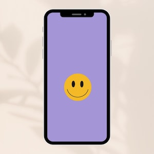 Op de afbeelding: Een smartphone met een zwart frame en een paars scherm met een gele smiley. De smiley heeft twee zwarte ogen en een gebogen zwarte mond. De telefoon staat tegen een neutrale achtergrond.