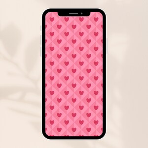Op de afbeelding: Een smartphone toont een roze en rood hartpatroon. Het ontwerp heeft een herhalend patroon van rode harten tegen een roze diamantachtergrond. De telefoon heeft een zwarte rand en een inkeping aan de bovenkant.
