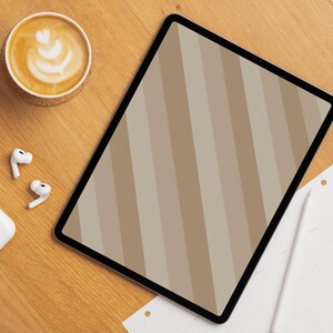 Può includere: Un tablet digitale con uno schermo a righe beige e marroni è appoggiato su una superficie di legno, accanto a una tazza di caffè con latte art, auricolari wireless e un blocco note. Lo schermo del tablet mostra un motivo a strisce diagonali.