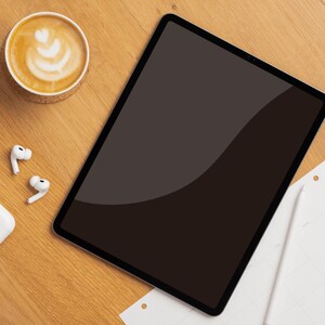 Puede incluir: Una tableta digital con pantalla negra descansa sobre una superficie de madera, junto a una taza de café con arte latte, auriculares inalámbricos blancos y un bloc de notas con un bolígrafo. La escena sugiere un espacio de trabajo o un momento de relajación.