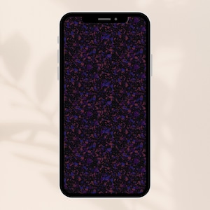 Op de afbeelding: Een smartphone toont een donker terrazzo patroon. Het ontwerp heeft een gespikkelde opstelling van paarse, blauwe en roze fragmenten tegen een zwarte achtergrond. De telefoon staat tegen een neutrale, gebroken witte achtergrond.