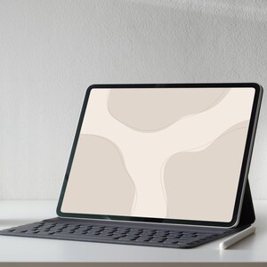 Op de afbeelding: Een zwarte tablet met een toetsenbordhoes en een stylus. Het scherm toont een beige abstract ontwerp met gebogen vormen en lijnen. De opstelling staat op een wit oppervlak tegen een witte muur.