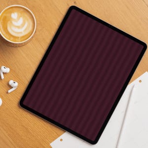 Op de afbeelding: Een tablet met een donker kastanjebruin scherm met een subtiel verticaal streeppatroon. Het apparaat ligt naast een witte stylus, een paar witte draadloze oordopjes en een kopje koffie met latte art op een oppervlak van licht houtnerf.