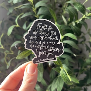 May include: Black and white sticker with a quote by Ruth Bader Ginsburg: "Fight for the things that you care about, but do it in a way that will lead others to join you."