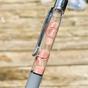 May include: A gray and silver pen with a clear barrel filled with small, brown football-shaped charms.