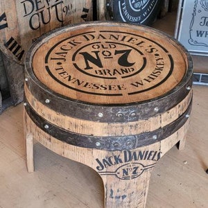 May include: A handcrafted wooden barrel table with the Jack Daniel's Old No. 7 Brand logo on the tabletop and base. The table is made from a repurposed whiskey barrel, with metal bands and a rustic finish.