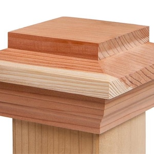 May include: A wooden post cap with a square top and a decorative molding around the bottom. The cap is made of natural cedar wood and has a light brown color.