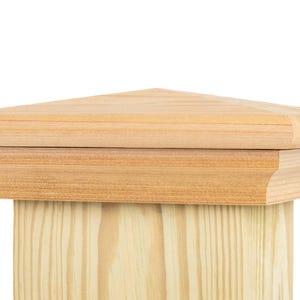 May include: A wooden post cap with a pyramid-shaped top. The cap is made of light-colored wood and has a decorative edge. The post it sits on is also made of light-colored wood.