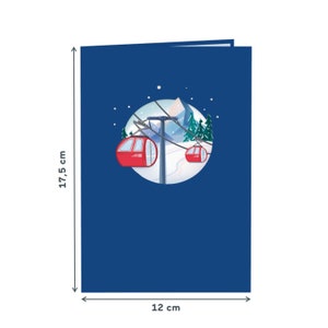 May include: A blue card with a pop-up design of a snowy mountain scene with two red cable cars. The card measures 12 inches by 17.5 inches.