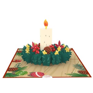 May include: A 3D pop-up card featuring a white candle with a flame, surrounded by a green wreath with red berries, gold stars, and pine cones. The card is on a brown background with a red border.
