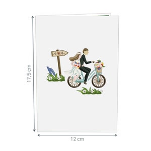 May include: A white card with a couple riding a blue bicycle with a basket of flowers. The sign above them reads "Mr. & Mrs.". The card measures 12 inches by 17.5 inches.