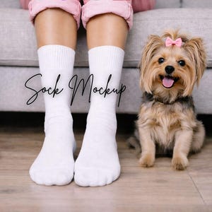May include: A pair of white socks with the text "Sock Mockup" in a script font. A small dog with a pink bow sits on the right. The person is wearing pink pants.