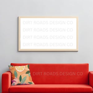 May include: A red sofa with a decorative pillow featuring a citrus fruit design. Above the sofa is a framed print with the text "DIRT ROADS DESIGN CO". The wall is painted a light gray color.
