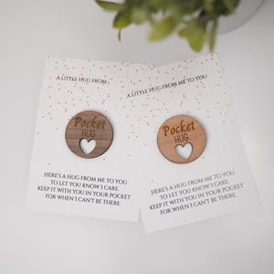 May include: Two cards with a wooden heart-shaped token that says "Pocket Hug" on it. The cards have a pink and white polka dot background and say "A little hug from me to you" and "Here's a hug from me to you to let you know I care. Keep it with you in your pocket for when I can't be there."